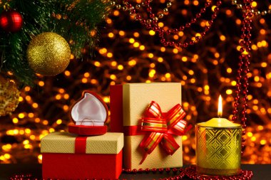 Noel ağacının köşesindeki altın çelenklerin Bokeh Noel arkaplanı. Noel ağacının altında parlak bir top, yüzüklü bir çanta ve bir mum..