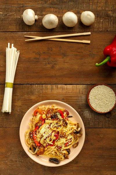 Udon con pollo e funghi in salsa thai pad in un piatto beige accanto al sesamo e udon. — Foto Stock