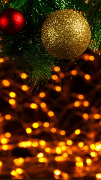 Bokeh Weihnachten Neujahr Hintergrund aus goldenen Girlanden auf schwarz in der Ecke eines Weihnachtsbaumzweiges mit einer glänzenden Kugel. — Stockfoto