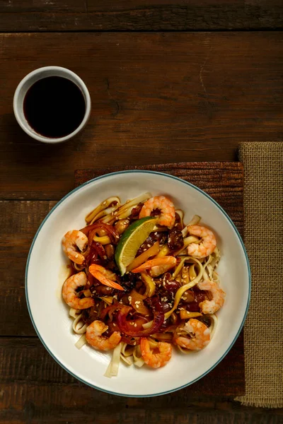 Mantarlı udon ve hafif bir tabakta karides peçete, çubuk ve malzemelerin yanında..