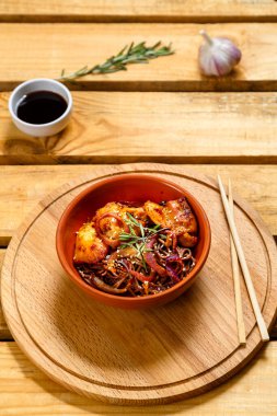 Soby tavuk ve susam tohumlarıyla ahşap bir stantta kil bir tabakta ve susam tohumları ve soya sosuyla ahşap bir masada soya sosunun yanında duruyor..