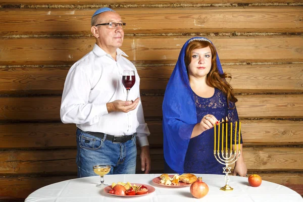在Rosh Hashanah前夕，犹太家庭的丈夫和妻子坐在餐桌前，一个男人为Kiddush的女人把酒点着蜡烛. — 图库照片