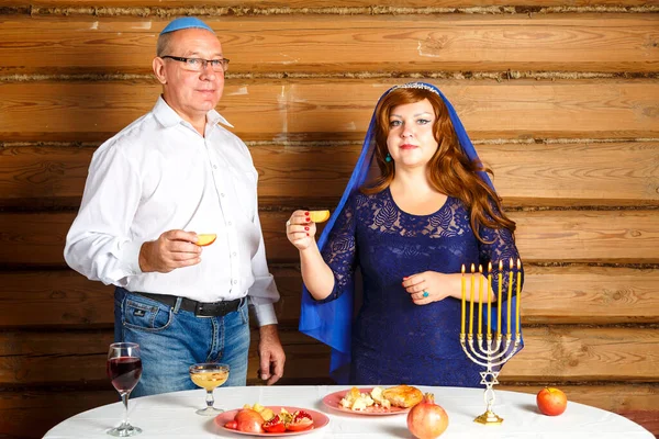 在Rosh Ashana，一个犹太家庭，一个穿着kippah的丈夫和一个头戴斗篷的妻子，在一个放着蜡烛的节日桌上吃蜂蜜沙拉. — 图库照片