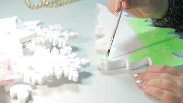 Une femme dans une pièce à la table fait des décorations de Noël pour la maison en peignant une figurine d'arbre de Noël avec aquarelle verte — Video