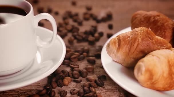 O ceașcă de cafea și croissante pe o masă cu o împrăștiere de boabe de cafea — Videoclip de stoc