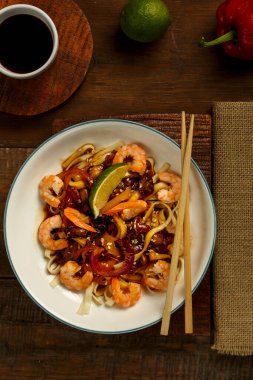 Mantarlı udon ve hafif bir tabakta karides peçete, çubuk ve malzemelerin yanında..