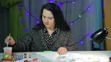 Masadaki bir kadın, kar taneleri ve suluboya yıldızlarla ev için Noel süslemeleri yapıyor.