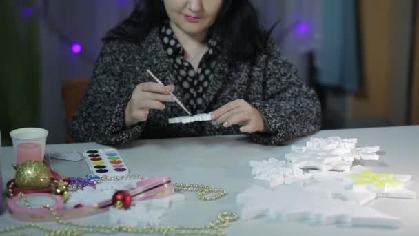 Una mujer joven en la mesa hace decoraciones caseras para Navidad pintando estrellas con pinturas de acuarela. — Vídeos de Stock