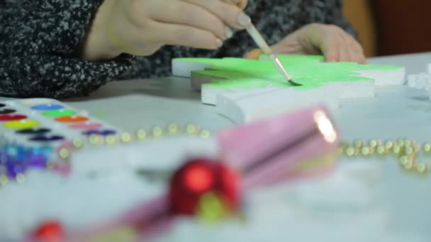Взимку ввечері молода жінка робить на Різдво прикраси, малюючи фігурку ялинки з зеленим аквареллю. — стокове відео