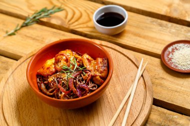 Teriyaki soslu tavuk ve susam tohumlarıyla birlikte ahşap bir stantta kil bir tabakta susam tohumlarının, otların ve soya sosunun yanında duruyor..