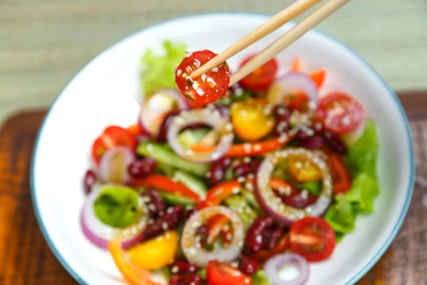 Piatto leggero con insalata di sesamo pan-asiatica e mano con bacchette sopra il piatto. — Foto Stock