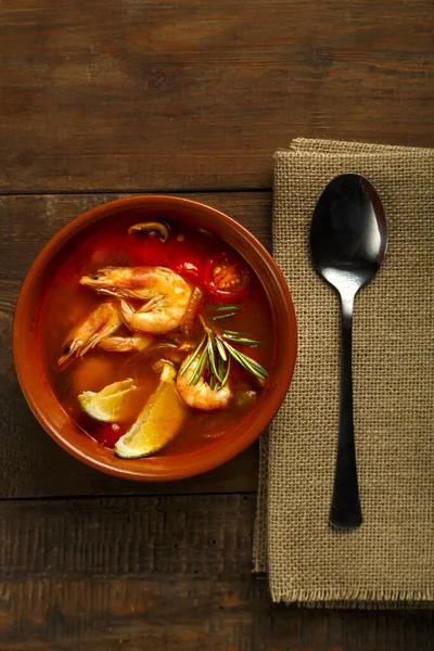 Sopa de ñame Tom con camarones y lima en un plato marrón sobre una mesa de madera junto a una cuchara en una servilleta. —  Fotos de Stock