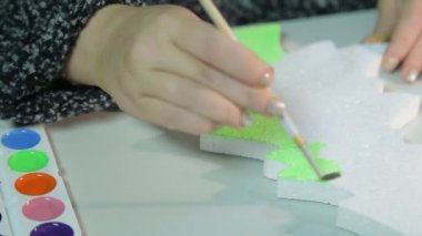 Masadaki bir kadın, yeşil suluboyalı bir Noel ağacı heykelciği yaparak ev için Noel süslemeleri yapıyor..