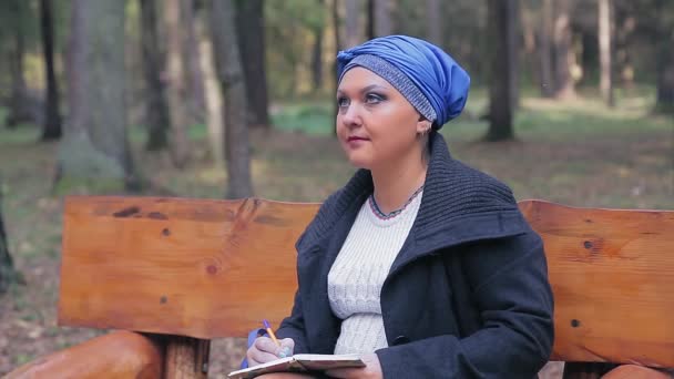 Une femme juive dans une coiffure bleue traditionnelle sur un banc dans une ruelle esquisse un dessin — Video