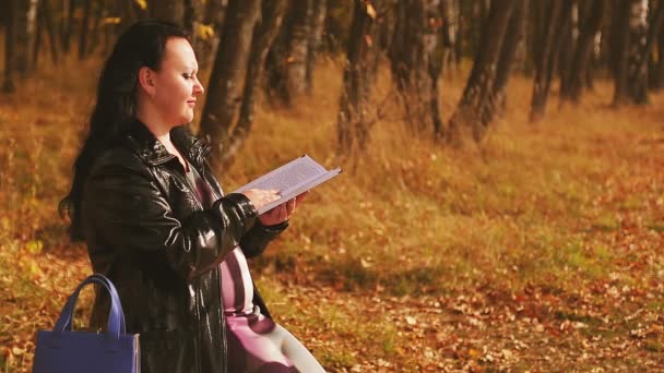 Una mujer embarazada en un callejón en un banco lee un libro. — Vídeos de Stock