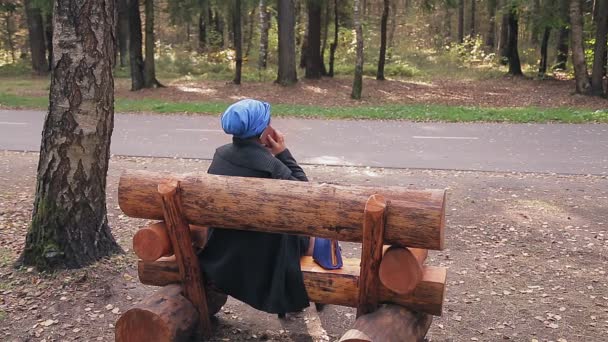 Mulher judia em uma cobertura para a cabeça tradicional em um banco em um parque de outono com as costas — Vídeo de Stock