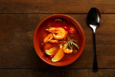 Tom tatlı patates çorbası, karides ve limonlu, kahverengi bir tabakta, tahta bir masanın üzerinde, kaşığın yanında..