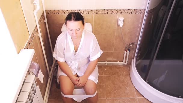 Жінка в білому халаті сидить в туалеті, стогін . — стокове відео
