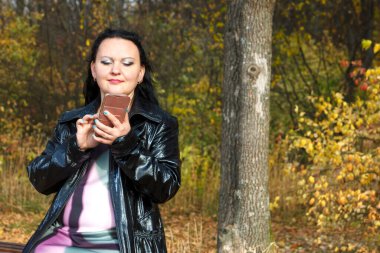 Sonbaharda parkta bankta oturan hamile bir kadın akıllı telefondan okuyor..