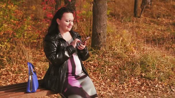 Eine schwangere Frau in einer Gasse auf einer Bank liest die Nachrichten auf einem Smartphone — Stockvideo