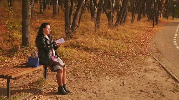 Uma mulher grávida num beco num banco lê um livro num dia ensolarado. — Vídeo de Stock
