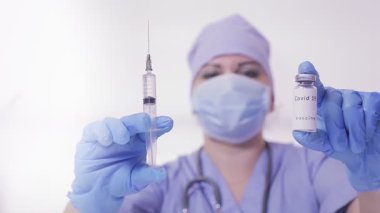Eldivenli ve maskeli bir doktor virüse karşı aşı yapıyor ve elinde bir şırınga var.