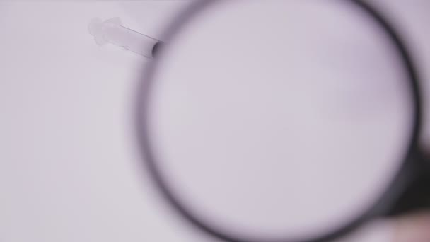 A vial with a vaccine against the virus is examined in a magnifying glass — Stock Video