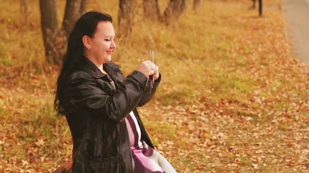 Een zwangere vrouw in een steeg op een bankje breit voor een ongeboren kind — Stockvideo