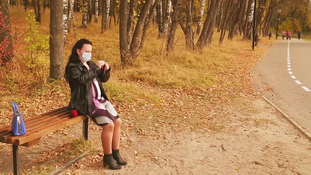 Těhotná žena v parku na lavičce v lékařské masce — Stock video