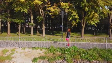 Kırmızı çizmeli, kahverengi saçlı ve kırmızı çantalı bir kadın güneşli bir günde sonbaharda bir ara sokakta yürüyor.