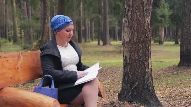 Une femme juive dans une coiffure bleue traditionnelle de profil sur un banc dans une ruelle lit un livre — Video