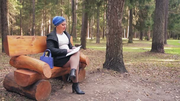 Jüdin mit traditioneller blauer Kopfbedeckung liest auf einer Bank in der Gasse ein Buch. — Stockvideo