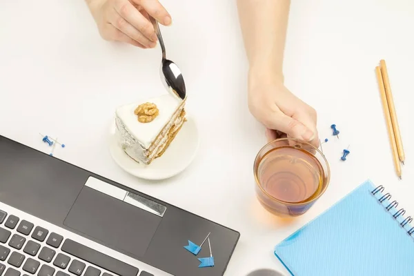 Girl drinking tea with piece of cake next to the laptop.