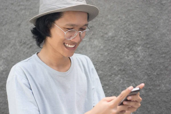 Attraente giovane asiatico uomo con cappello e occhiali utilizzando smartphone — Foto Stock
