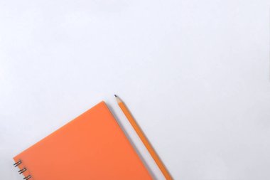 Design concept - Top view of orange spiral notebook and color pencil collection on white background. clipart