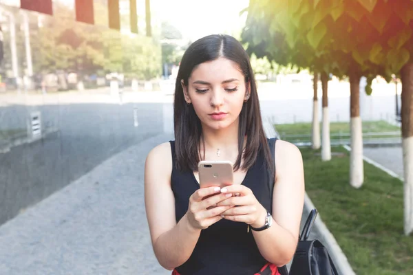 Chica feliz mensajes de texto en un teléfono inteligente apoyado en la pared de mármol en la ciudad . — Foto de Stock