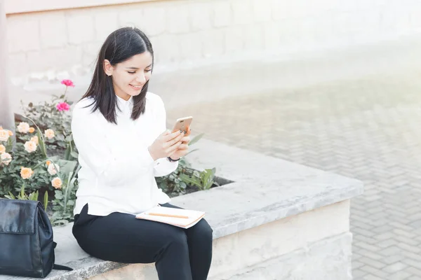 Onnellinen tyttö opiskelija käyttää älypuhelinta kaupungin lähellä yliopistoa . — kuvapankkivalokuva