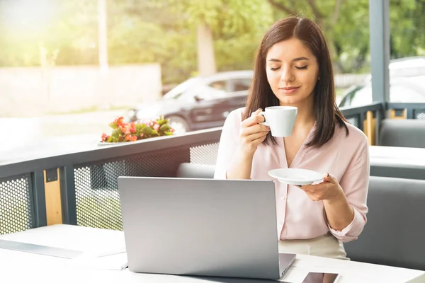 Pausa para café. Jovem mulher bonita segurando xícara de café e mantendo os olhos fechados enquanto sentado em seu local de trabalho — Fotografia de Stock