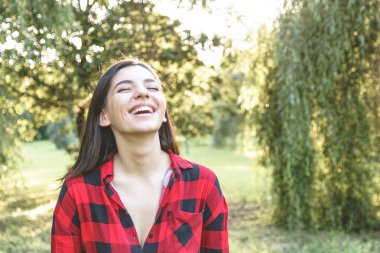 Kırmızı ekose gömlekli parkta gülümseyen mutlu kadın