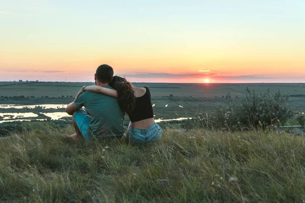 Couple is hugging and sitting close on a hill at sunset — Stock Photo, Image