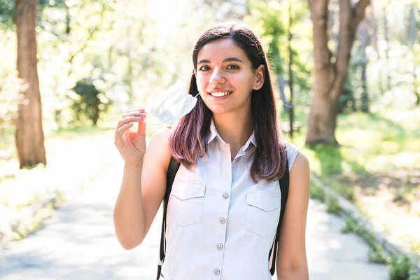 Vapauden tunne. Nuori nainen yksin puistossa poistaa lääketieteellinen naamio ja hengittää iloisesti — kuvapankkivalokuva