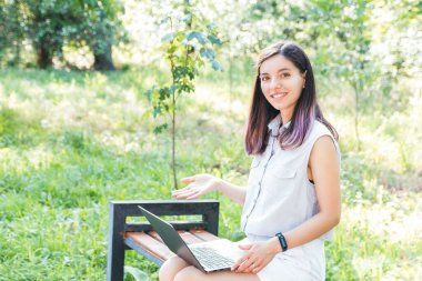 Parkta dizüstü bilgisayarda uzaktan öğrenen neşeli genç öğrenci sosyal mesafeyi koruyor ve yalnız zaman geçirmenin tadını çıkarıyor.