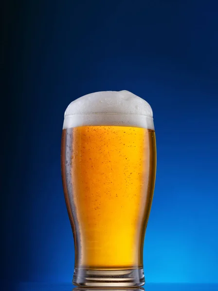 नीले पृष्ठभूमि पर प्रकाश बीयर के साथ ग्लास — स्टॉक फ़ोटो, इमेज