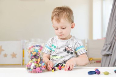 Küçük bir çocuk boncuk ve diğer küçük oyuncaklar ile oynuyor. Çocuk Bahçesi veya oyun eğlence merkezi