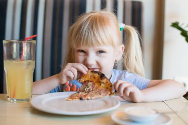 Mutlu bir kız bir kafe ve bir taze yapılmış pizza Salam ile yemek masada oturur. Uzun sarı saçları.