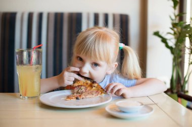 Mutlu bir kız bir kafe ve bir taze yapılmış pizza Salam ile yemek masada oturur. Uzun sarı saçları.