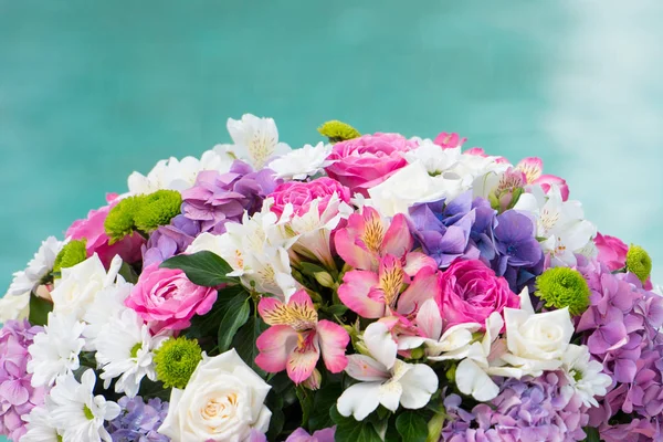 a beautiful bouquet in a box lies on the edge of a pool with blue water