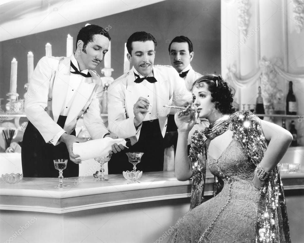 Two overly attentive waiters light a woman's cigarette and pour her drink