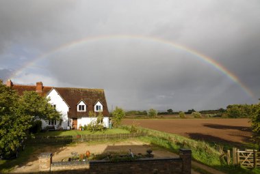 Buckingham, UK - September 11, 2017. A traditional English house is framed by a rainbow over countryside in Buckinghamshire, UK clipart