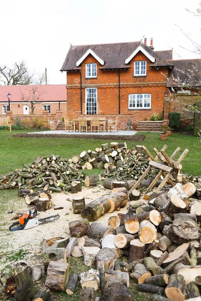 Cutting firewood with a chainsaw in an English garden setting with a large country house in the background